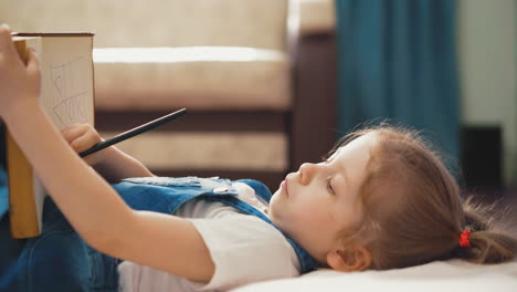 funny little child draws in book with pencil lying on floor