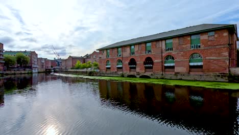 smooth daytime pan along a river in leeds, showing historic brick buildings, modern apartments, and reflections in calm water under cloudy skies