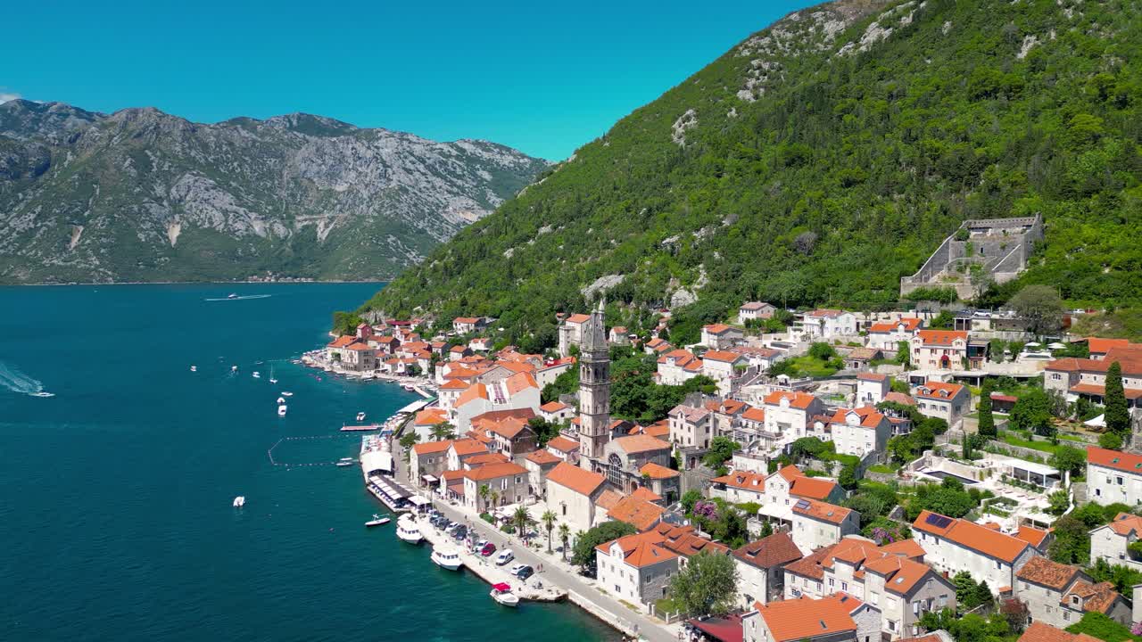 Aerial drone view of Perast city. Situated in Montenegro is a famous travel destination. View of Church of San Nicholas. Panoramic top view of costal city. Drone backwards and panning right.
