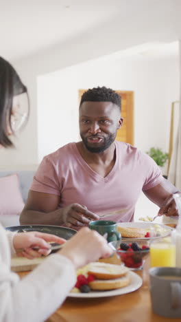 vertical video of happy diverse couple at table having breakfast