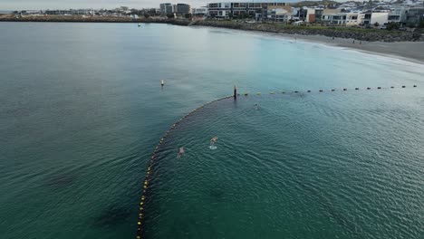 Drohne-Umkreist-Aufnahme-Eines-Schwimmers-Während-Einer-Sportübung-Im-Meer-Während-Des-Sonnenaufgangs-Innerhalb-Der-Schutzzone-–-Luxusvilla-Und-Strand-Von-Perth-City-Im-Hintergrund