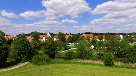 Blauer-Himmel-Mit-Weißen-Wolken,-Rote-Dächer-Von-Häusern-Und-Der-Stadtpark-Mit-Der-Schönen-Farbluftaufnahme-Der-Brücke