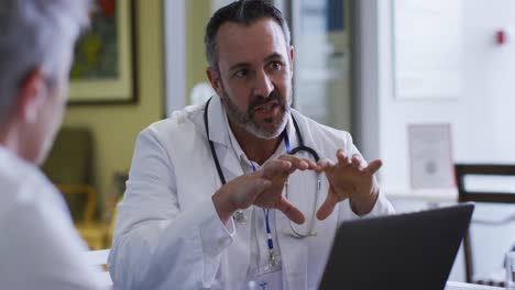 caucasian male doctor using laptop sitting and addressing hospital colleagues at a meeting