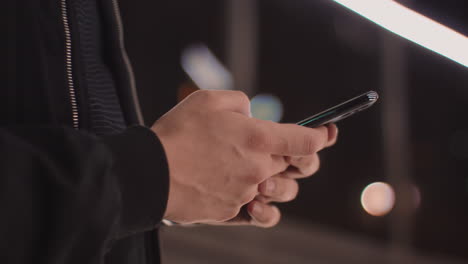 detail shot with hands of a man writing-texting a message on the phone in the city at night