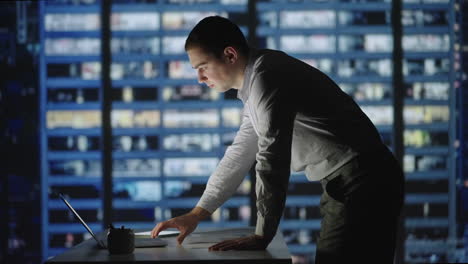 confident manager working late night in office. man standing in office lean over desk working on laptop. architects working on construction project