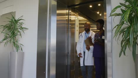 african american male and female doctors holding clipboard and tablet, talking at hospital