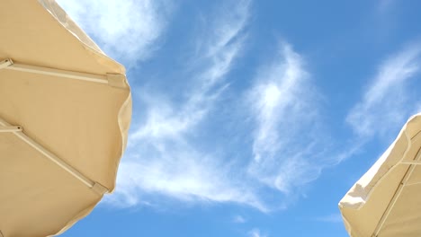 looking up towards two beach umbrellas against blue sky with clouds