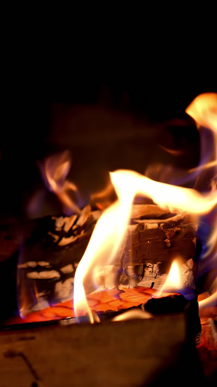 Fireplace with burning fire. Firewood combustion in fire at night. Warmth and comfort at home. Cozy fireplace in winter. Close-up. Vertical video