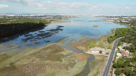 drone shot of swampland and river beside road with cars during sunny day in seixal,portugal