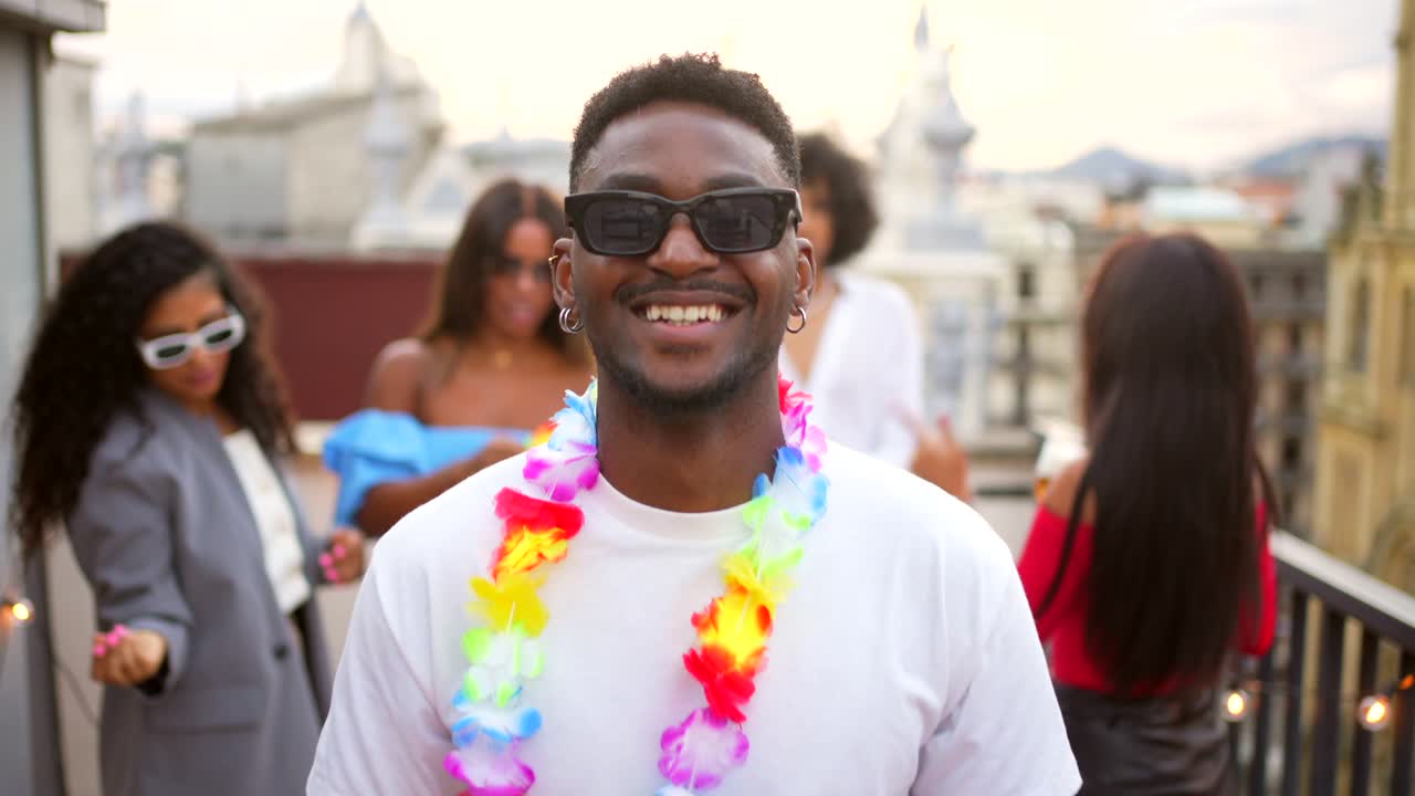 Jovem negro sorrindo e aproveitando uma animada festa em um terraço com amigos