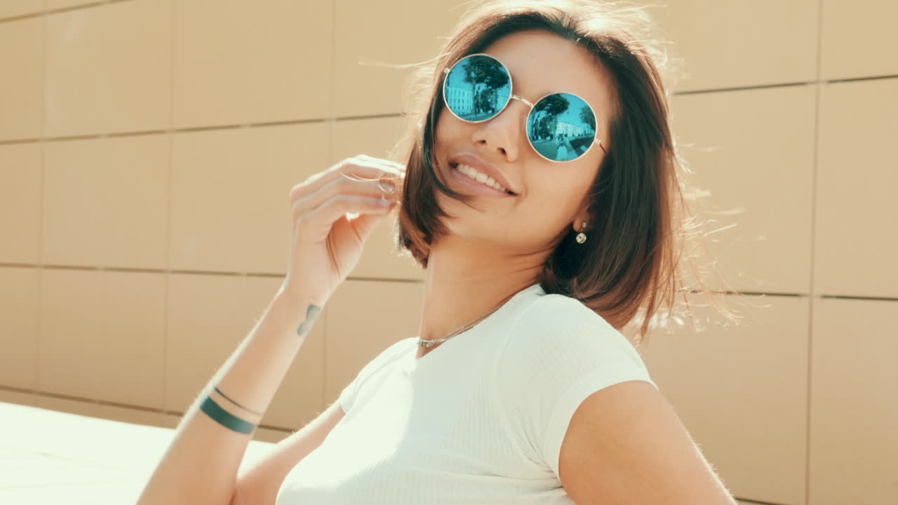 женщина в круглых солнцезащитных очках улыбается на открытом воздухе