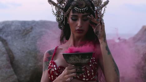 close up of beautiful, young belly dancer performing rhythmic hand movements by holding pink color smoke bomb, on the beach. slow motion