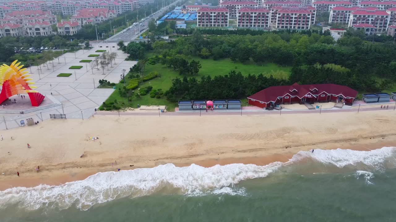 Mesmerizing sliding aerial view of ocean waves on natural sandy beach shoreline with yellow and red crossed fingers monument and green park