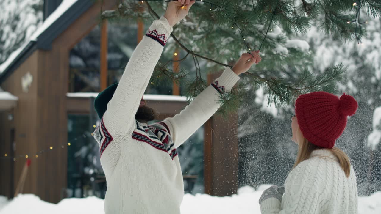кавказская пара украшает сад на рождество в огнях на открытом воздухе.