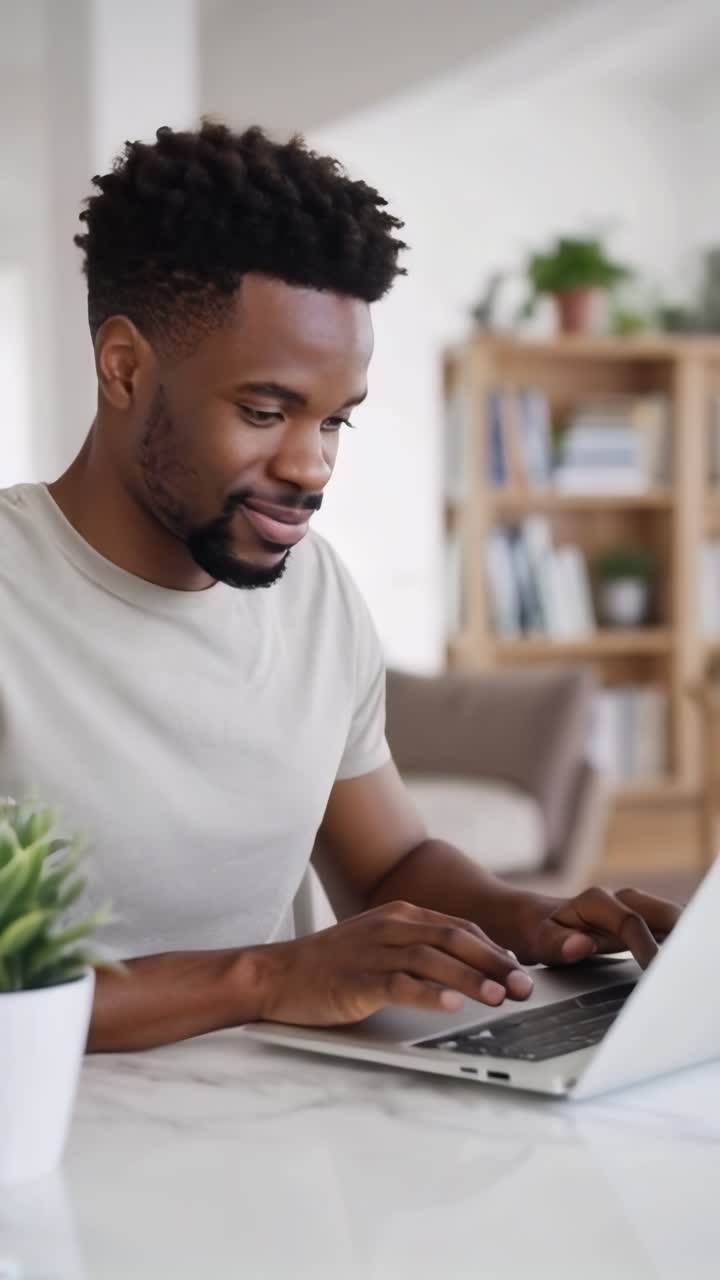 Afro young male typing on a laptop working in his home office.