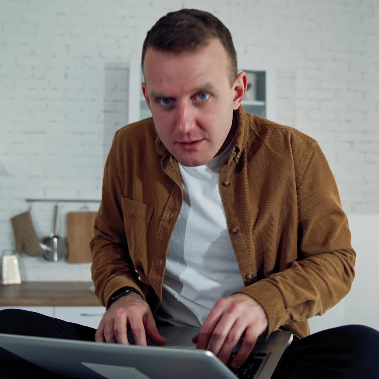 Funny comic businessman working at home. Mad face of a young freelancer looking on camera angrily while sitting on a kitchen table with a laptop