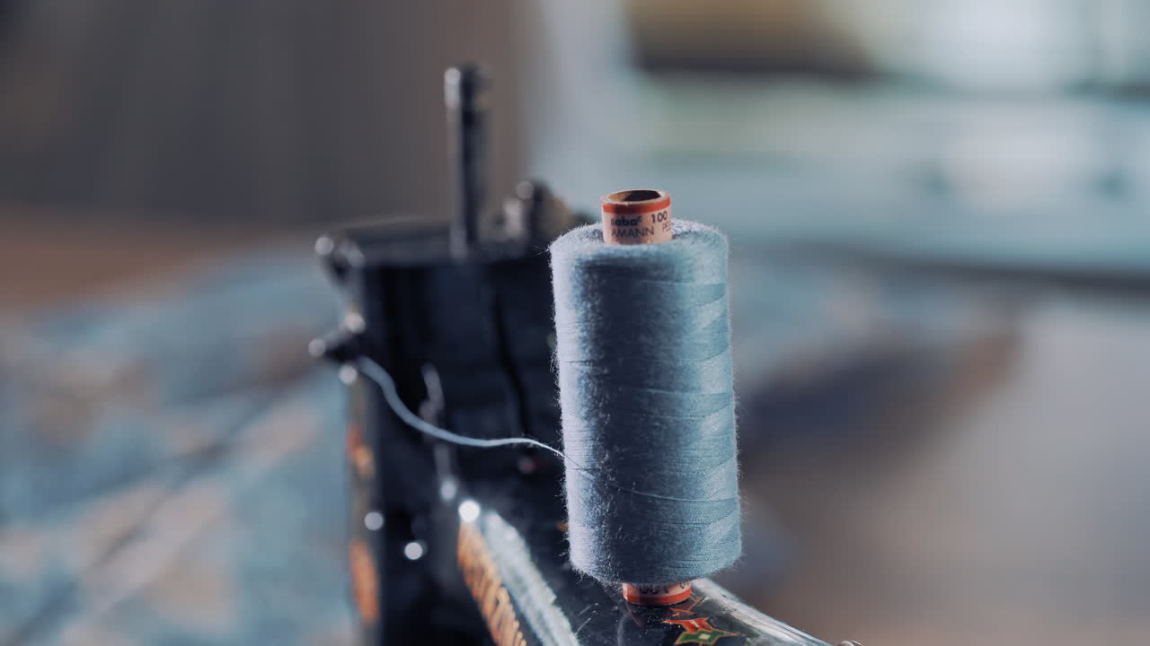 Close-up of a bobbin of blue thread on the sewing machine spinning. Cotton reel spinning on sewing machine for making dress in atelier. Slow motion.