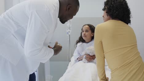 Diverse-doctor-examining-sick-girl-patient-with-stethoscope-with-her-mother-in-slow-motion