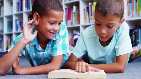 escolares acostados en el suelo y leyendo un libro en la biblioteca de la escuela