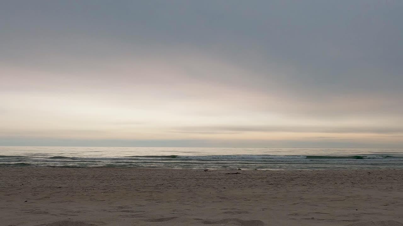 Peaceful beach scene at Smiltynė, Lithuania, with soft waves and pastel sky at sunset