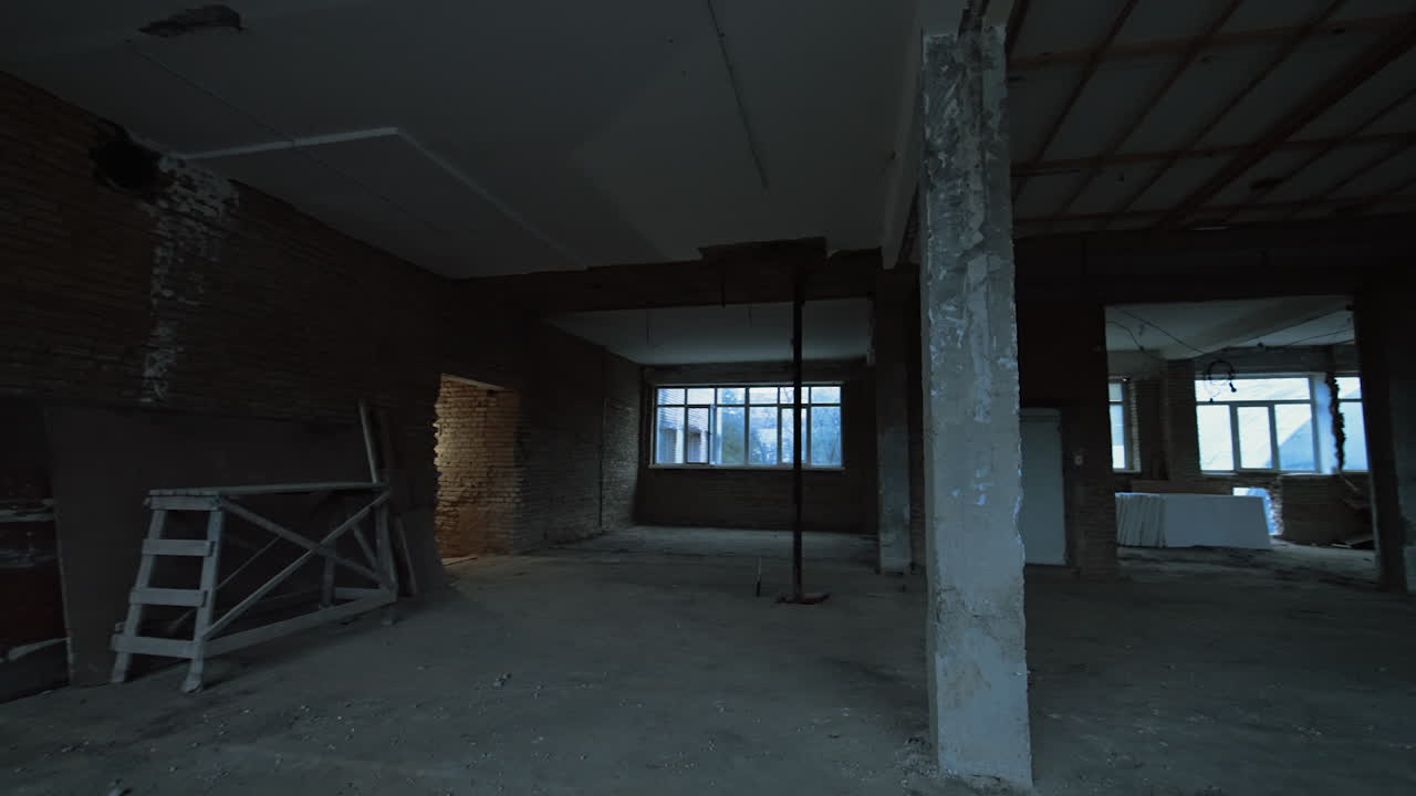 Walking around by the big spacious room in the building under the construction. Unfinished premise with columns.