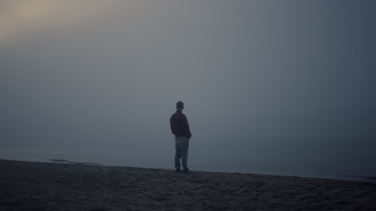 hombre tranquilo de pie en la playa en el mar. tipo soñador disfrutando del paisaje oceánico