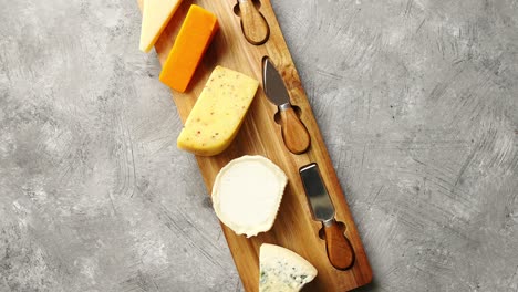 assortment of various kinds of cheeses served on wooden board with fork and knives