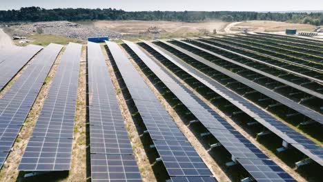 Plano-Amplio-De-Paneles-Solares-A-Baja-Altitud,-Reflejos-Del-Sol-En-Los-Paneles-Con-Movimiento-Dinámico-Sobre-Un-Fondo-De-Cielo-Azul