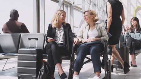 businesswoman sitting in airport departure with female colleague in wheelchair talking together