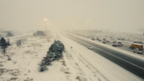 Vista-Aérea-De-La-Carretera-Con-Tráfico-Lento-Moviéndose-A-Través-De-Ventisca-De-Nieve-En-Toronto-Con-Poca-Visibilidad-En-Ontario,-Canadá