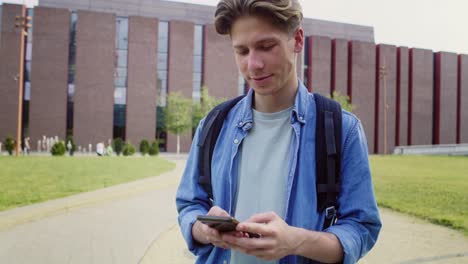 caucasian male student browsing phone while sitting on campus