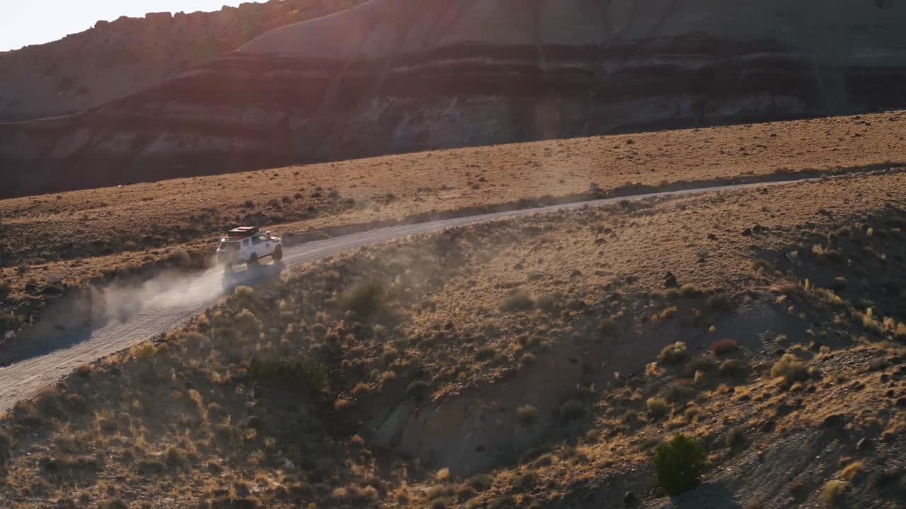 유타의 벤토나이트 언덕을 가로질러 먼지로 가득 찬 도로를 운전하는 색 4x4 트럭의 공중 사진