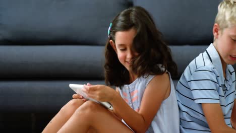 siblings sitting back to back and using digital tablet in living room