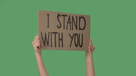 showing cardboard poster with inscription i stand with you. human rights demonstration. hands holding a poster a green screen, chroma key. close up. slow motion