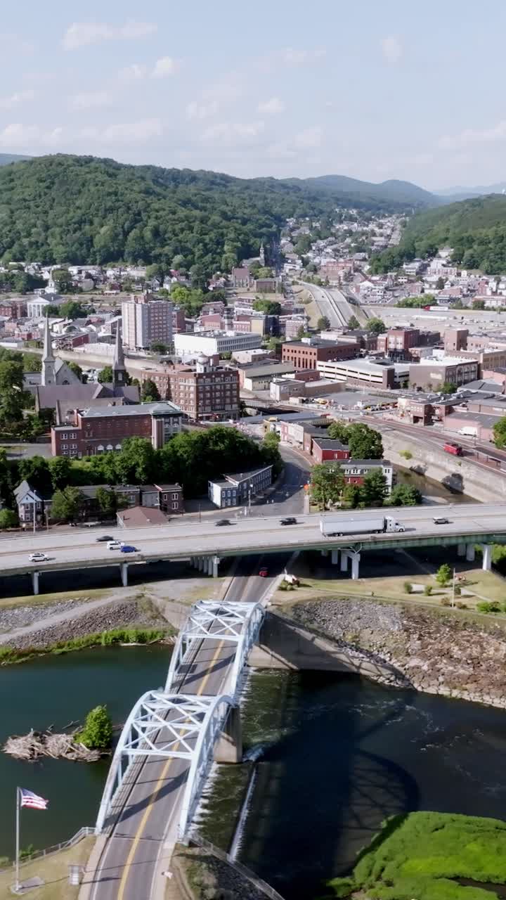 Ripresa aerea verticale con drone che si sposta da sinistra a destra sopra Cumberland, Maryland, mostrando l'architettura della città e il paesaggio circostante alla luce del giorno.