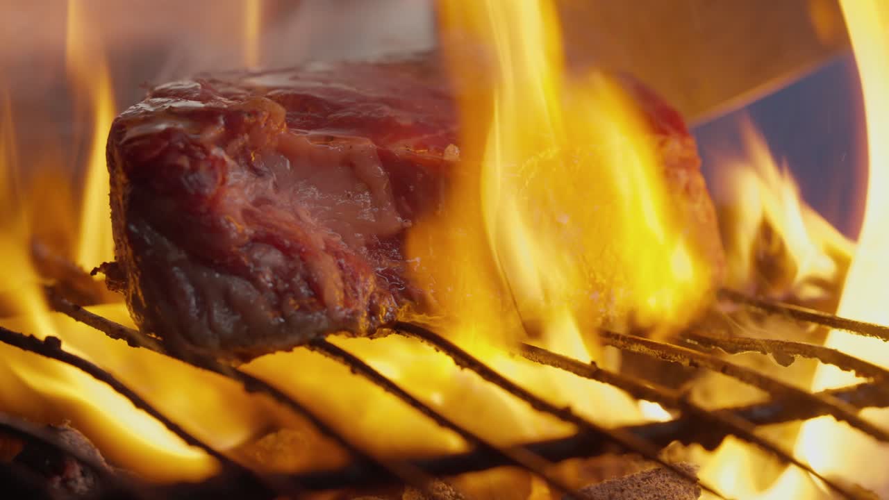 un cocinero convierte un bistec a la parrilla en medio de llamas, humo y brasas de barbacoa