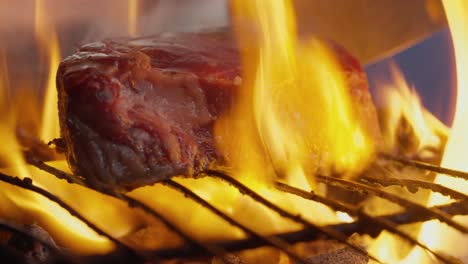 A-cook-turns-a-grilled-steak-amid-flames,-smoke-and-barbecue-coals