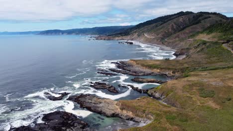 4.000-Imágenes-Aéreas-De-30-Fps-En-La-Costa-De-Oregon---Disparo-De-Un-Dron-En-Ascenso-De-La-Ruta-Estadounidense-101---Las-Olas-Del-Océano-Chocan-Contra-Formaciones-Rocosas-Junto-Al-Océano-Mientras-La-Gente-Viaja-Por-Carretera-Por-El-Paisaje-Natural-épico-De-La-Carretera-Real