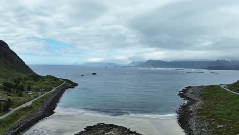Aerial reverse dolly over Rorvik Beach in Lofoten, Norway revealing Road E10 to Henningsvaer curving around beach on left and right