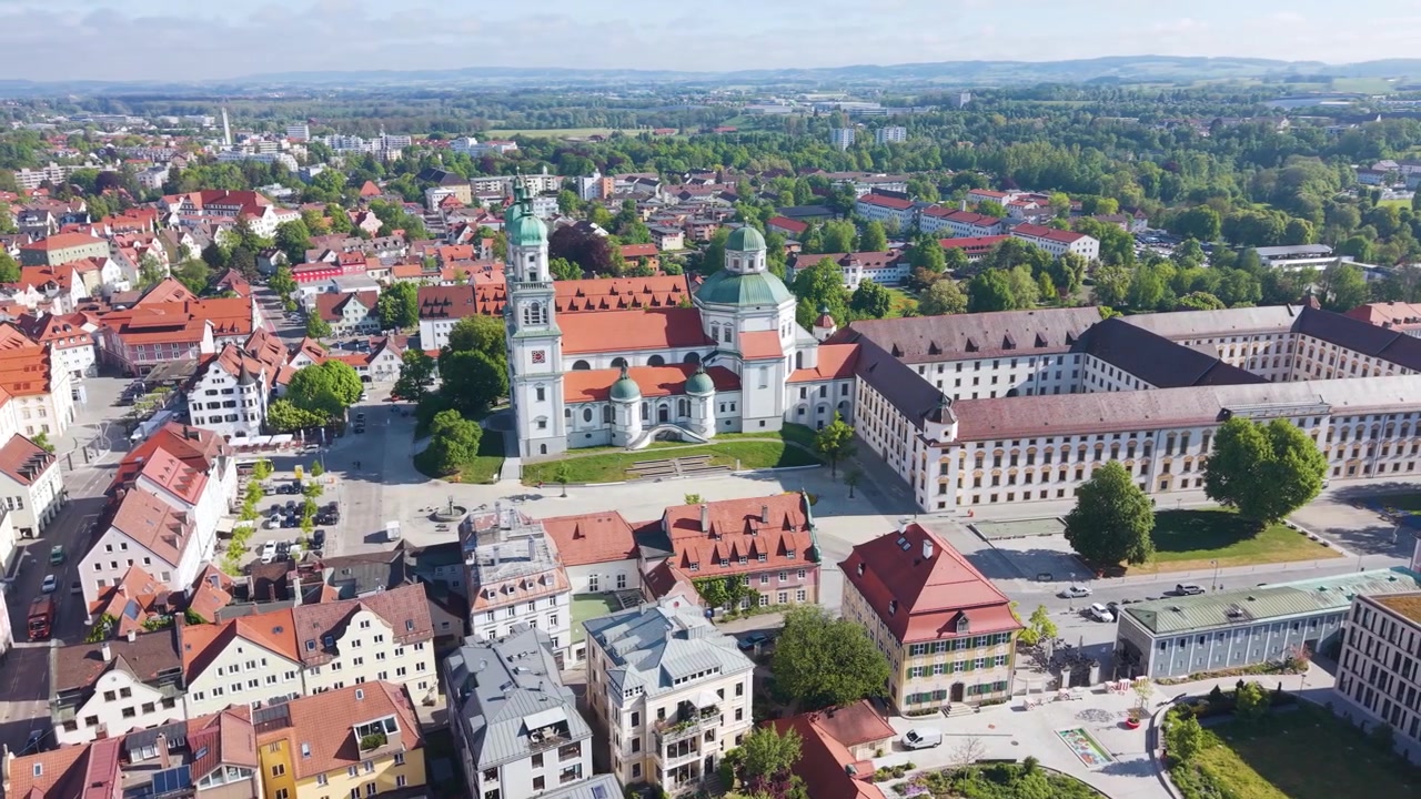 Ripresa aerea orbitante della Basilica di San Lorenzo a Kempten Allgäu, Germania, con architettura storica, tetti rossi e la piazza cittadina circostante in Baviera. UHD