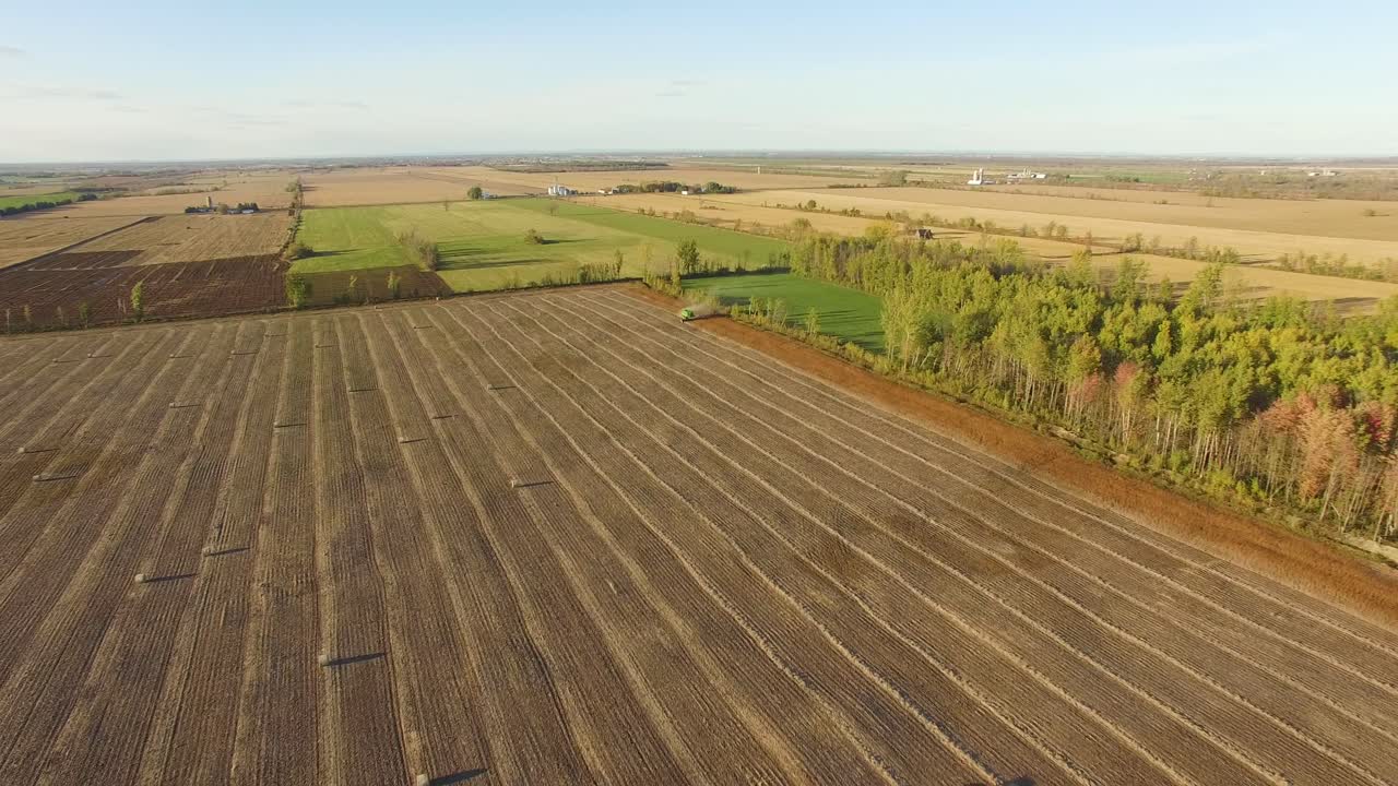 High angle, wide aerial view of farmland as tractors work in the field