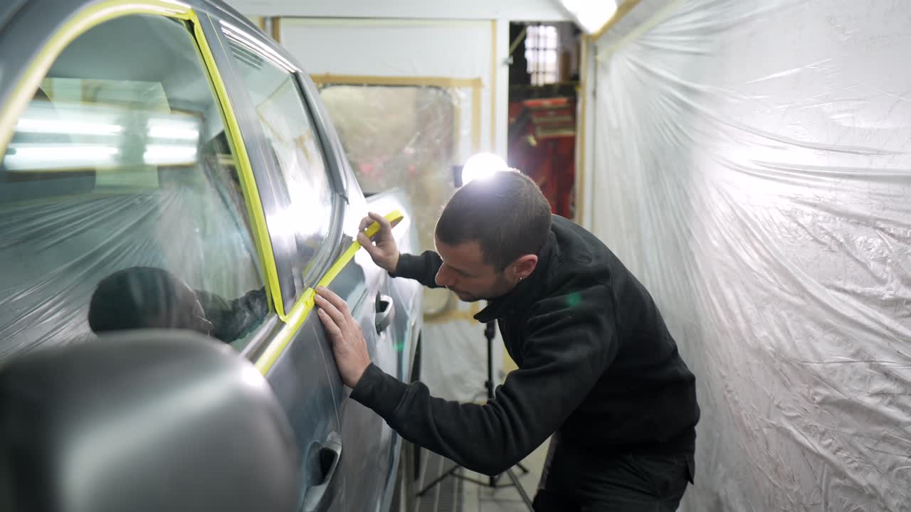 Mann klebt Autoscheibe mit Klebeband in einer Autowerkstatt ab