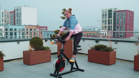 athletic woman riding on spinning stationary bike training routine on house rooftop, weight loss