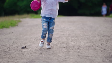 happy child is running in summertime. beautiful little girl in stylish jeans holds pink handbag and runs joyfully outdoors in summer.