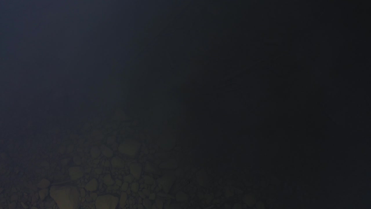 imágenes aéreas de arriba hacia abajo del fondo rocoso de un lago claro y frío que vuela hacia arriba y lejos mientras el fondo desaparece en la oscuridad