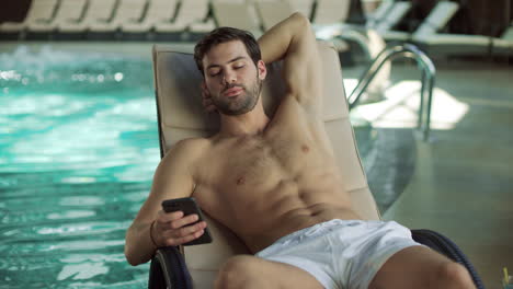 Closeup-cheerful-man-using-mobile-at-poolside.-Happy-man-relaxing-with-phone