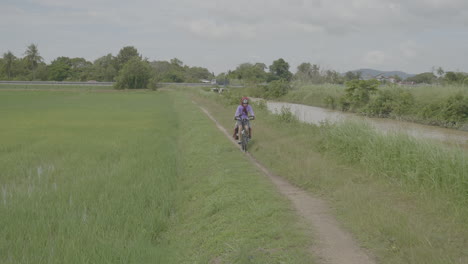 lone female bikes on dirt path in grassy field of alor setar malaysia