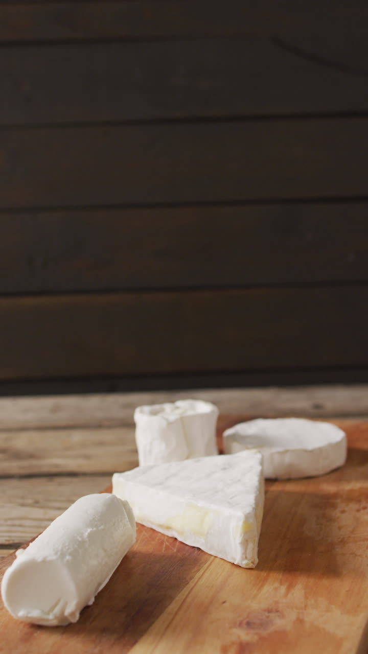 video vertical de algunos tipos de queso fresco en una tabla de cortar de madera y un fondo rústico