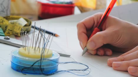 the fashion designer is developing the design of a new dress.young woman fashion designer is drawing a pattern of a new model of a dress. close-up of a hand of a young woman fashion designer, she is engaged in cutting a new model of a dress