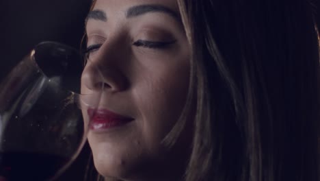 Close-up-of-beautiful-brunette-woman-drinking-red-wine-in-a-dark-room,-slow-motion